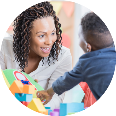 Woman playing blocks with small child in school setting
